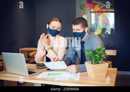 Business people with face masks working together on laptop in modern coworking office Stock Photo