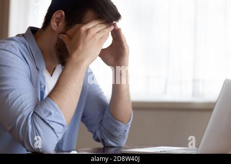 Exhausted young male employee sitting at workplace tired from work Stock Photo