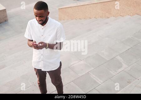 Young bearded African businessman in white shirt and brown pants messaging Stock Photo