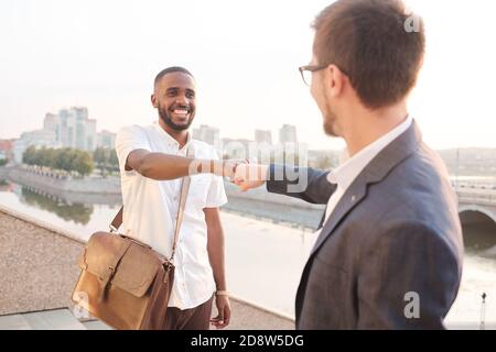 Two young happy business partners of various ethnicities making punch bump Stock Photo