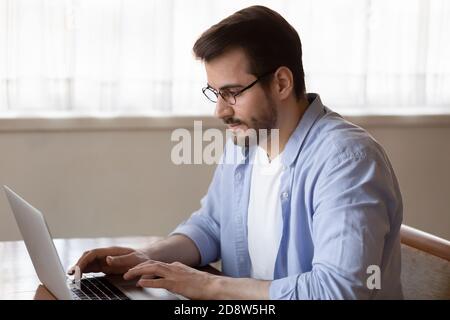 Focused millennial man working at home typing message on laptop Stock Photo
