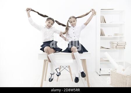 Successful team. Little schoolgirls classmates kids. Schoolgirls friends sit on desk. Best friends relaxing. Schoolgirls tidy hairstyle relaxing having rest. School uniform. Rebellious spirit. Stock Photo