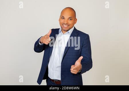 Portrait of a successful young African American businessman guy pointing his fingers at the camera with a happy and funny face. Good energy and vibes. Standing on a gray background Stock Photo