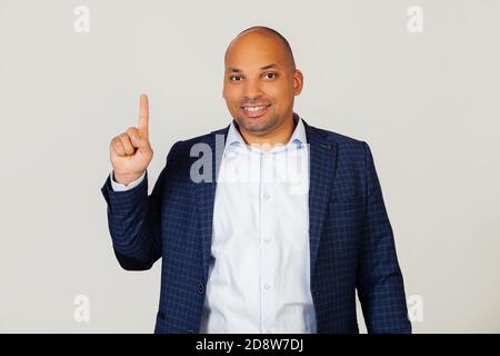 Portrait of successful young African American businessman guy, showing number one fingers, smiling, confident and happy. The man shows one finger. Number 1 Standing on a gray background Stock Photo