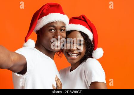 Beautiful black man and woman in Santa hats taking selfie Stock Photo