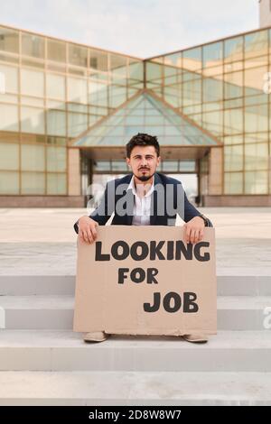 Young bearded man holding piece of cardboard with notice of looking for job Stock Photo