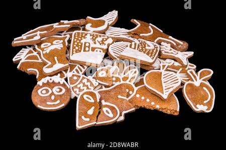 Heap of broken and bitten Christmas gingerbreads isolated on a black background. Close-up of damaged baked holiday cookies decorated by white frosting. Stock Photo