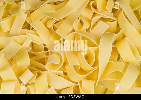 Yellow egg pasta texture of wavy wide noodles. Raw flat ribbon tagliatelles rolled of wheat dough in beautiful background of Italian or Asian cuisine. Stock Photo