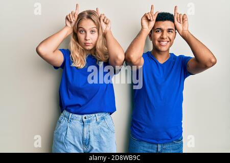 Young interracial couple wearing casual clothes doing funny gesture with finger over head as bull horns Stock Photo