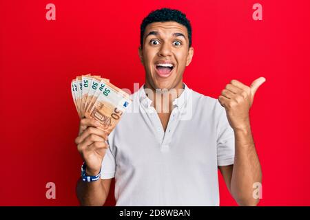 Young arab man holding 50 euro banknotes pointing thumb up to the side smiling happy with open mouth Stock Photo