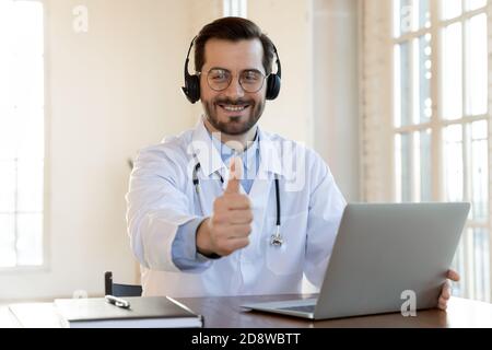 Happy doctor in wireless earphones recommending contact to medical hotline Stock Photo