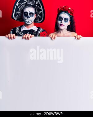 Young couple wearing mexican day of the dead costume holding blank empty banner thinking attitude and sober expression looking self confident Stock Photo