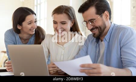 Diverse group of smiling coworkers sitting at laptop doing paperwork Stock Photo
