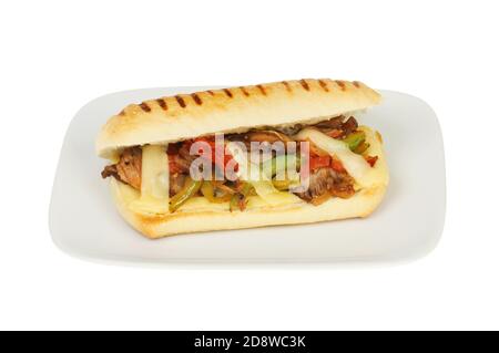 Beef, onion, pepper, tomato and emmental cheese in a panini on a plate isolated against white Stock Photo