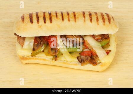 Beef, onion, pepper, tomato and emmental cheese in a panini on a wooden chopping board Stock Photo