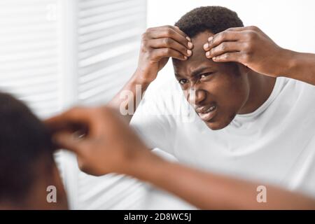 Worried Black Man Examining Face Looking At Wrinkles In Bathroom Stock Photo