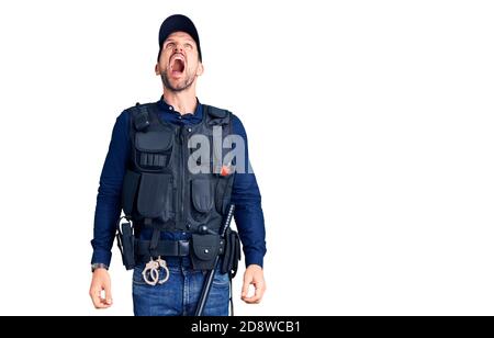 Young handsome man wearing police uniform angry and mad screaming frustrated and furious, shouting with anger. rage and aggressive concept. Stock Photo