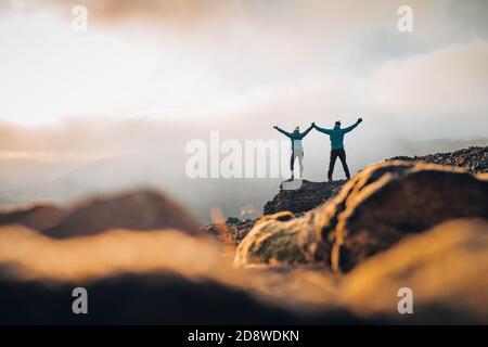 Couple travelers Man and Woman standing on cliff relaxing mountains and clouds aerial view Love and Travel happy emotions Lifestyle concept. Young Stock Photo