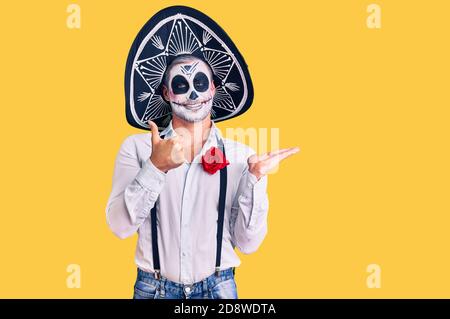 Man wearing day of the dead costume over background showing palm hand and doing ok gesture with thumbs up, smiling happy and cheerful Stock Photo