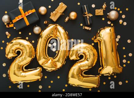 2021 balloon gold text on black background with golden confetti, Christmas gift boxes, gold balls, festive decor. Happy New year eve invitation with Stock Photo