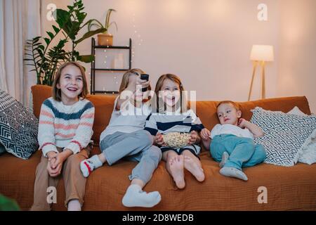 Laughing children sitting on a couch, watching television, eating popcorn Stock Photo