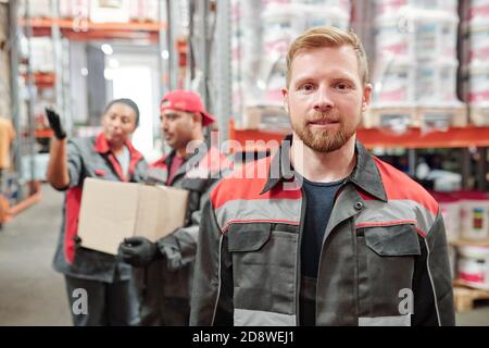 Successful young bearded man in workwear looking at you against colleagues Stock Photo