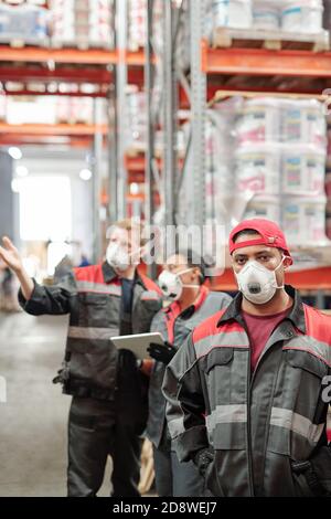 Serious middle aged Latino male worker in uniform and protective respirator Stock Photo