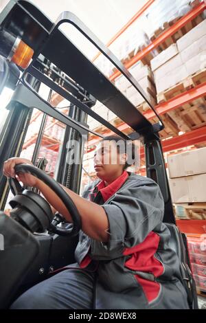 Young mixed-race female in workwear sitting by steer inside industrial machine Stock Photo