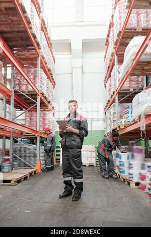 Serious young male manager of warehouse in uniform using digital tablet Stock Photo