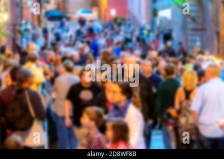 A blur of a crowd of people at dusk. People are gathered on a street between buildings. People are blurred enough not to be recognizable. Stock Photo