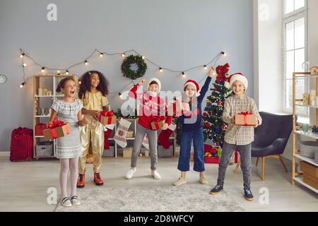 Mixed race children's friends jump together, holding presents and rejoicing that Christmas has come. Stock Photo