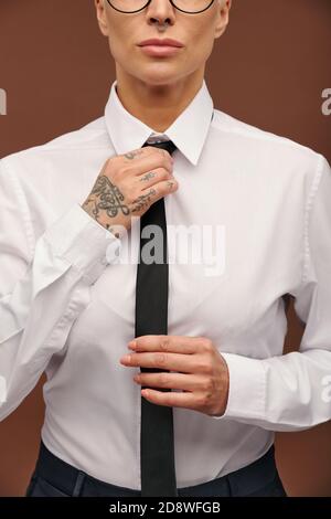 Serious middle aged businesswoman in white shirt putting on black necktie Stock Photo