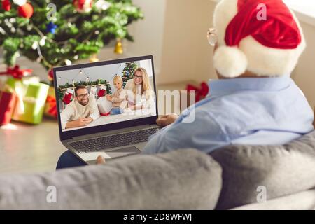 Senior man grandfather in Santa festive hat sitting on sofa and communicating with family online at Christmas Stock Photo