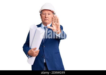 Senior handsome grey-haired man wearing architect hardhat holding blueprints with open hand doing stop sign with serious and confident expression, def Stock Photo