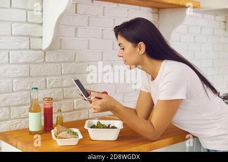 Woman having lunch ordered in meal delivery and using mobile to leave review or to count calories Stock Photo