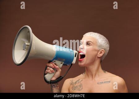 Very angry female with tattoos on arm, chest and neck shouting in megaphone Stock Photo