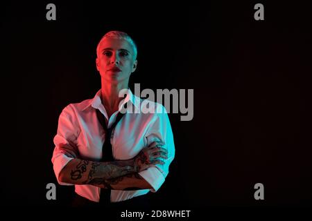 Elegant manlike woman in white shirt, black tie and pants crossing arms on chest Stock Photo