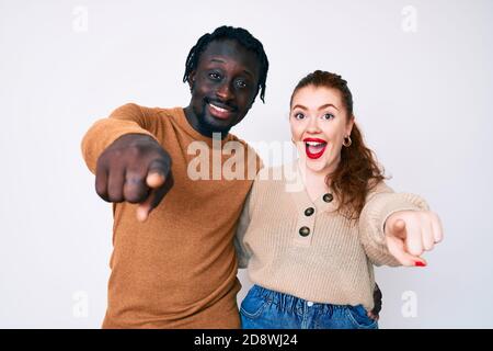 Interracial couple wearing casual clothes pointing to you and the camera with fingers, smiling positive and cheerful Stock Photo