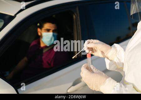 Doctor doing a PCR test COVID-19 on a patient through the car window. PCR diagnostic for Coronavirus presence,doctor in PPE holding test kit Stock Photo