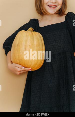 Cropped image of a girl in a black dress, holding pumpkin. Dressed for halloween Stock Photo