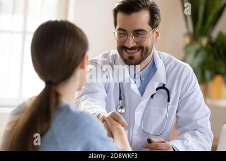 Pleasant smiling male doctor meeting young woman patient at clinic Stock Photo