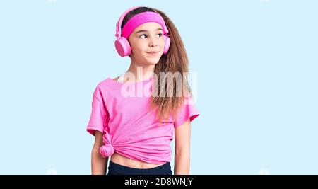 Cute hispanic child girl wearing gym clothes and using headphones smiling looking to the side and staring away thinking. Stock Photo