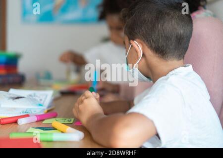 Boy painting in preschool classroom wearing face protective mask - Back to school during coronavirus outbreak concept - Focus on kid's ear Stock Photo