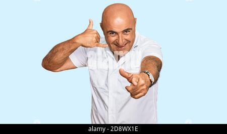 Mature middle east man with mustache wearing casual white shirt smiling doing talking on the telephone gesture and pointing to you. call me. Stock Photo