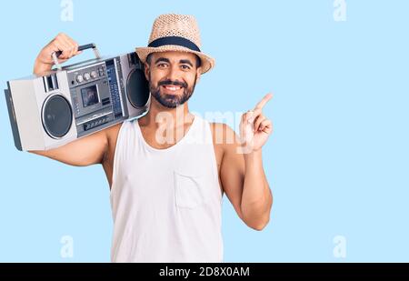 Young hispanic man holding boombox, listening to music smiling happy pointing with hand and finger to the side Stock Photo