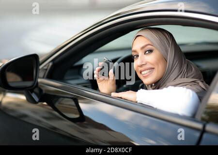 Young muslim lady showing auto keys, sitting on driver's seat Stock Photo