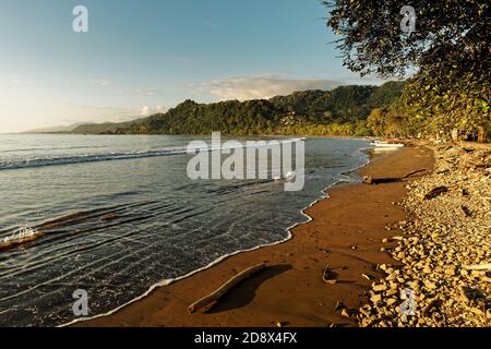 Pacific coast of Costa Rica in Central America, evening sunset with palm trees, ocean and clouds on the red sky. Stock Photo