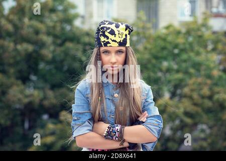 Confident teenager. Young woman teenage girl with folded arms and long light brown hair standing outside city park green tree on background. Model in Stock Photo