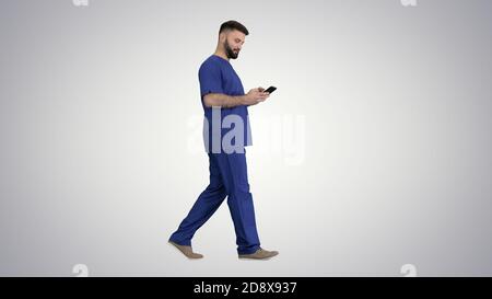 Wide shot. Side view. Surgeon doctor walking and using his phone on gradient background. Professional shot in 4K resolution. 044. You can use it e.g. Stock Photo