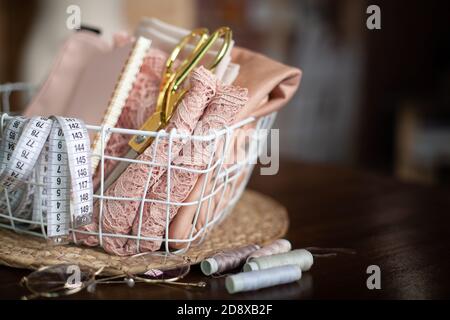 Sewing tools of tailoring scissors, tape measure, pink lace fabric in mesh basket and thread spools Stock Photo